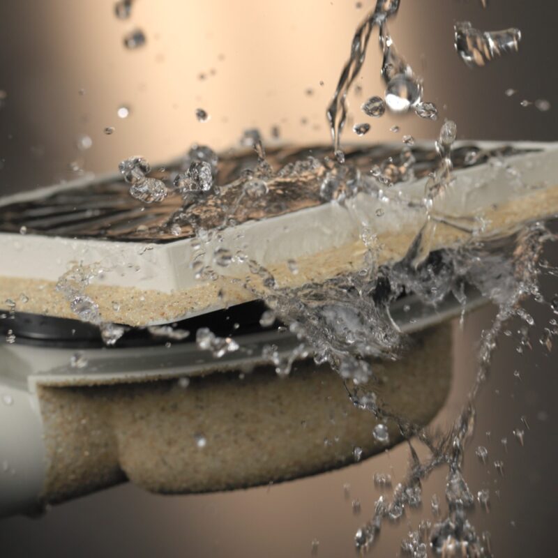 Close-up van een doucheput met zijuitlaat en verstelbare opties. De werking van de doucheput wordt geïllustreerd door er water op te gooien.