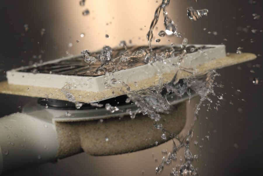 Close-up van een doucheput met zijuitlaat en verstelbare opties. De werking van de doucheput wordt geïllustreerd door er water op te gooien.